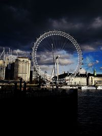 Ferris wheel at amusement park against cloudy sky