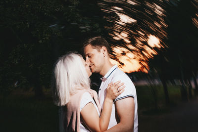 Couple kissing while standing trees at dusk