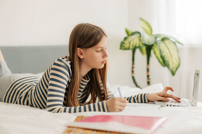 Portrait of a cute girl student preparing for lectures using a laptop, making notes in a notebook. 