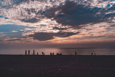 Silhouette people on beach against sky during sunset