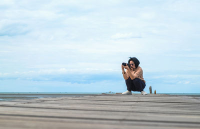 Woman photographing at beach against sky