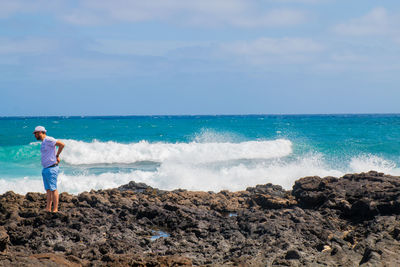 Man standing on rock at beach against sky