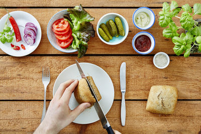 Cropped hands of man cutting bread in plate on table 