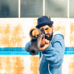 Man holding gun while standing against wall