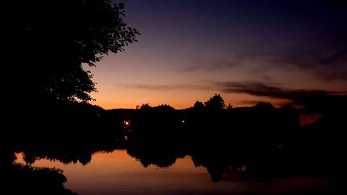 Silhouette trees by lake against romantic sky at sunset