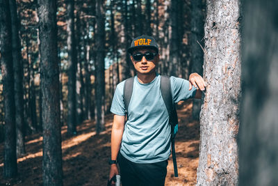 Full length of boy standing by tree trunk in forest