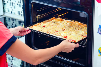Close-up of person putting pizza into oven
