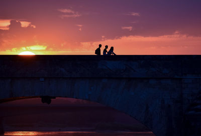 Silhouette of young friends on a colorful sunset when returning home, crossing a bridge.