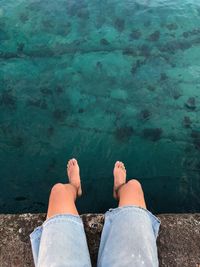 Low section of man sitting on retaining wall over lake