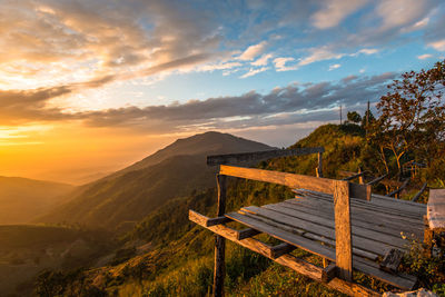 Empty bench on landscape against sky during sunset