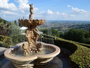 Fountain in formal garden by landscape against sky