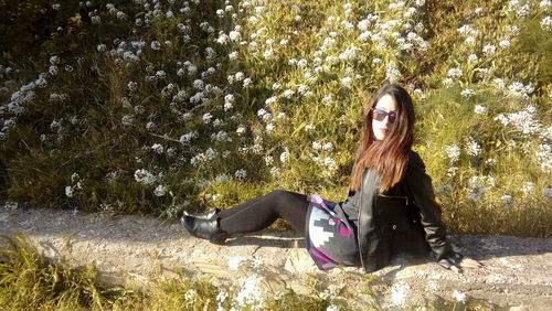 Side view of woman sitting on concrete by wildflowers