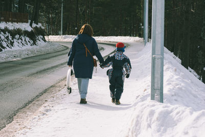 Full length of mother and son holding hands while walking on road during winter