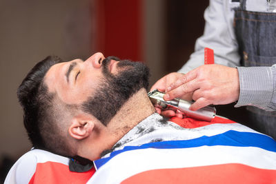 Midsection of barber shaving male customer beard in salon