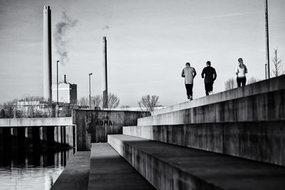 Rear view of joggers on pier against sky