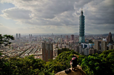 Woman photographing taipei 101 tower while crouching on rock