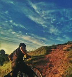 Rear view of man riding bicycle on road against sky