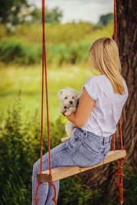 Young woman with a white dog on a tree swing.