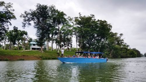 People in boat by trees against sky