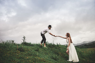 Young couple standing on field against sky