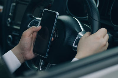 Midsection of businessman using mobile phone while driving car