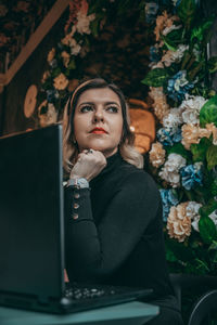 Portrait of young woman using phone while sitting on plant