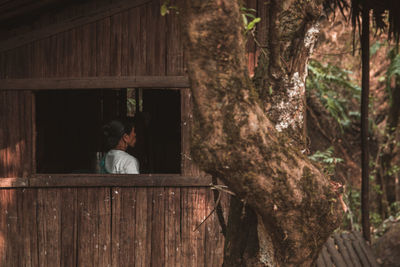 Rear view of woman sitting on wood against trees