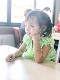 Portrait of cute girl sitting on table at home