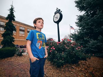 Boy standing by tree against sky