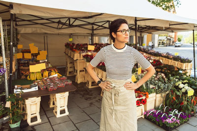 Thoughtful female owner standing with hands on hip outside flower shop