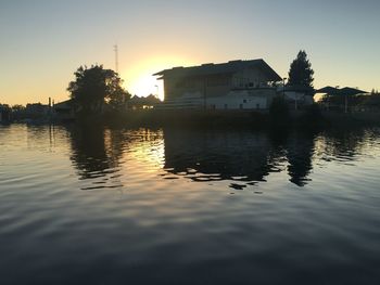 Silhouette buildings by lake against sky during sunset