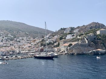 Sailboats in sea by buildings against clear sky