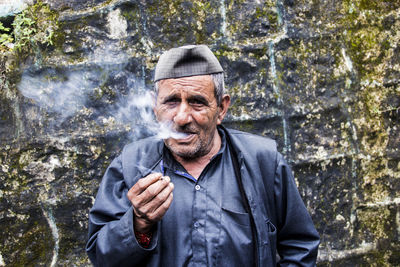 Portrait of senior man smoking bidi against weathered wall