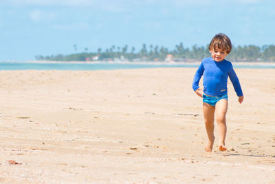 Cute boy walking at beach against sky on sunny day