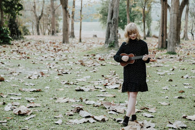 Smiling young woman playing ukulele while standing on field