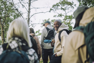 Portrait of smiling man wearing hooded shirt while hiking with friends in forest