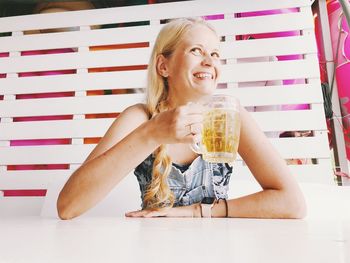 Smiling woman holding alcoholic drink while sitting at table in restaurant