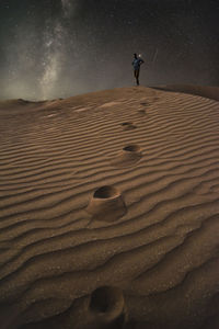 Low angle view of man standing at desert against star field