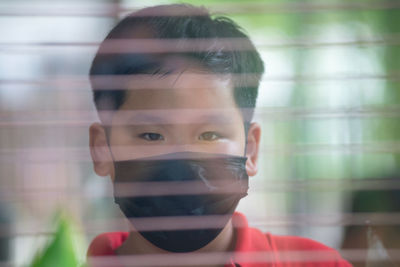 Close-up portrait of boy wearing mask seen through window