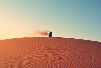 Man sitting on sand dune against clear sky