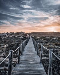 Boardwalk leading towards sea against sky during sunset