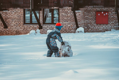 Rear view of boy playing on snow covered yard during winter
