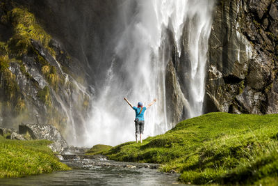Figure standing in front of waterfall spray, in green nature landscape