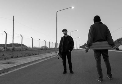 Male friends holding skateboard while standing on road