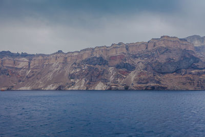 Scenic view of sea by mountain against sky