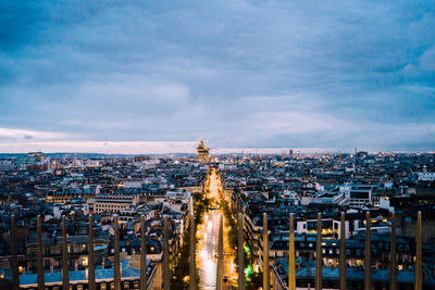 High angle view of city lit up against cloudy sky