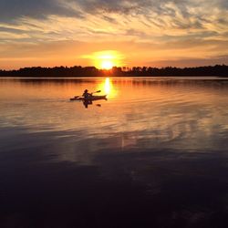 Rear view of person kayaking in calm lake at sunset