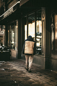 Rear view of man walking on footpath against building