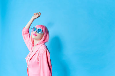 Low angle view of woman with arms raised against blue background