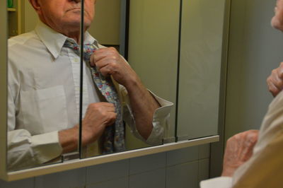 Cropped image of senior man adjusting necktie while looking in mirror